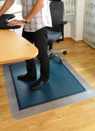 Person står på en blå yogamatta på ett kontorsgolv bredvid ett skrivbord och en kontorsstol