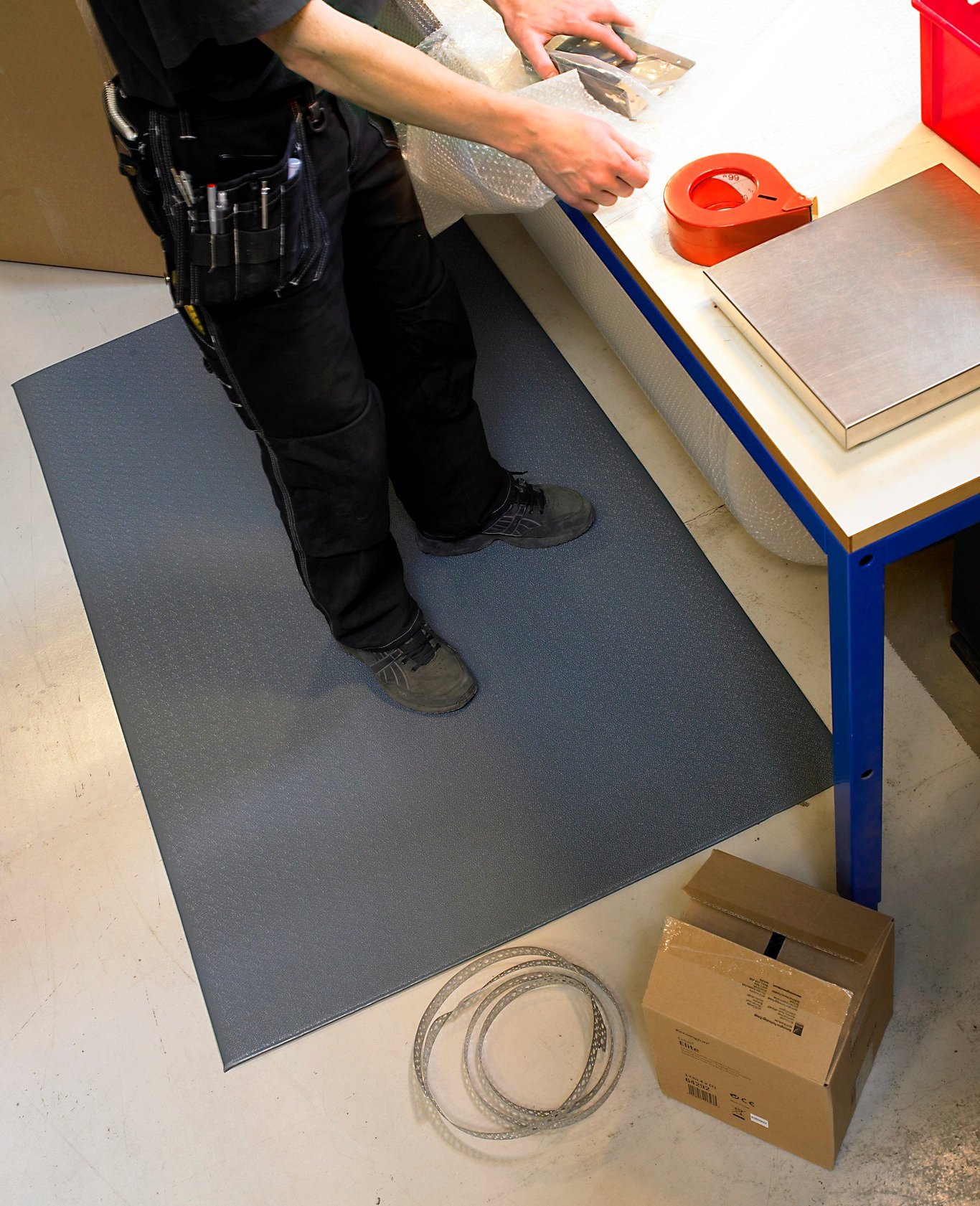 Person placerar en grå arbetsplatsmatta Matting Yoga Super Plus 61x91cm på golvet vid ett arbetsbord
