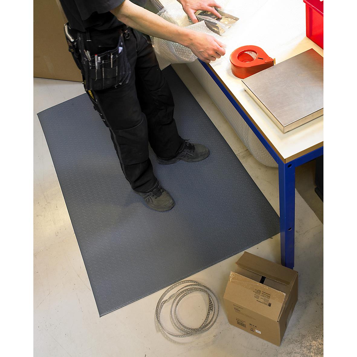 Person placerar en grå arbetsplatsmatta Matting Yoga Super Plus 61x91cm på golvet vid ett arbetsbord