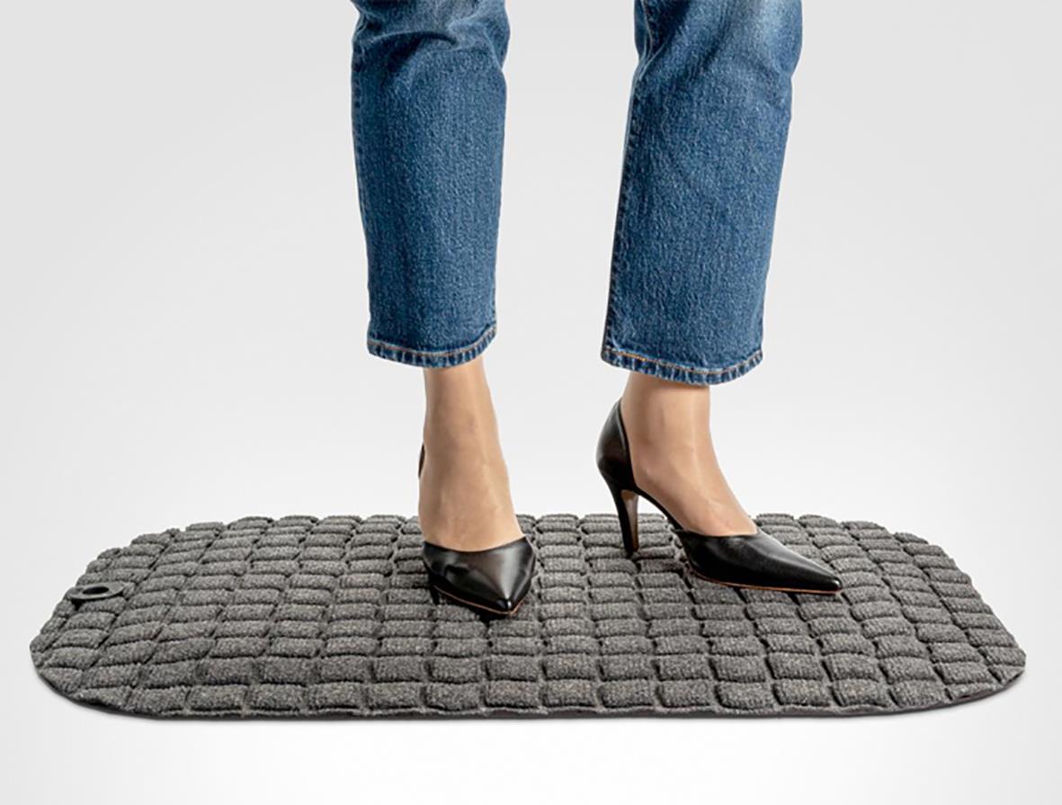 Person står på en grå arbetsplatsmatta med brickmönster, storlek 77 x 54 cm, i ett kontorsliknande miljö