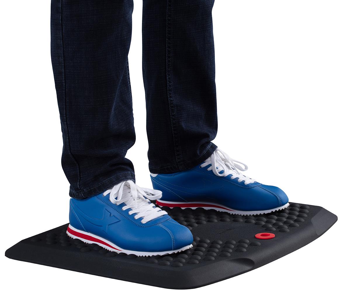 Person står på Sun-Flex StandMat Boost med blå skor, svart matta med knopp för stabilitet