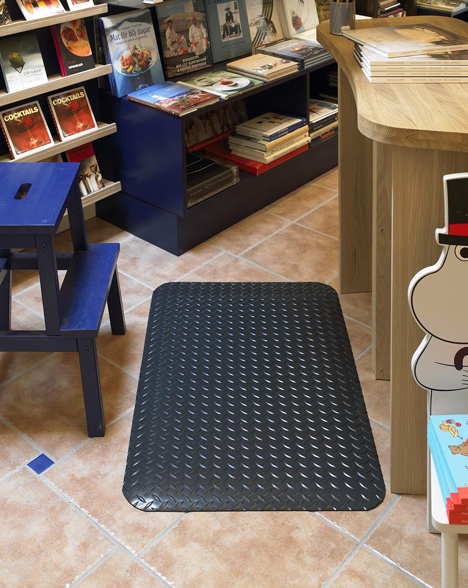 Svart arbetsplatsmatta Yoga Deck Zedlan 91x61cm på golvet i ett rum med bokhyllor och möbler