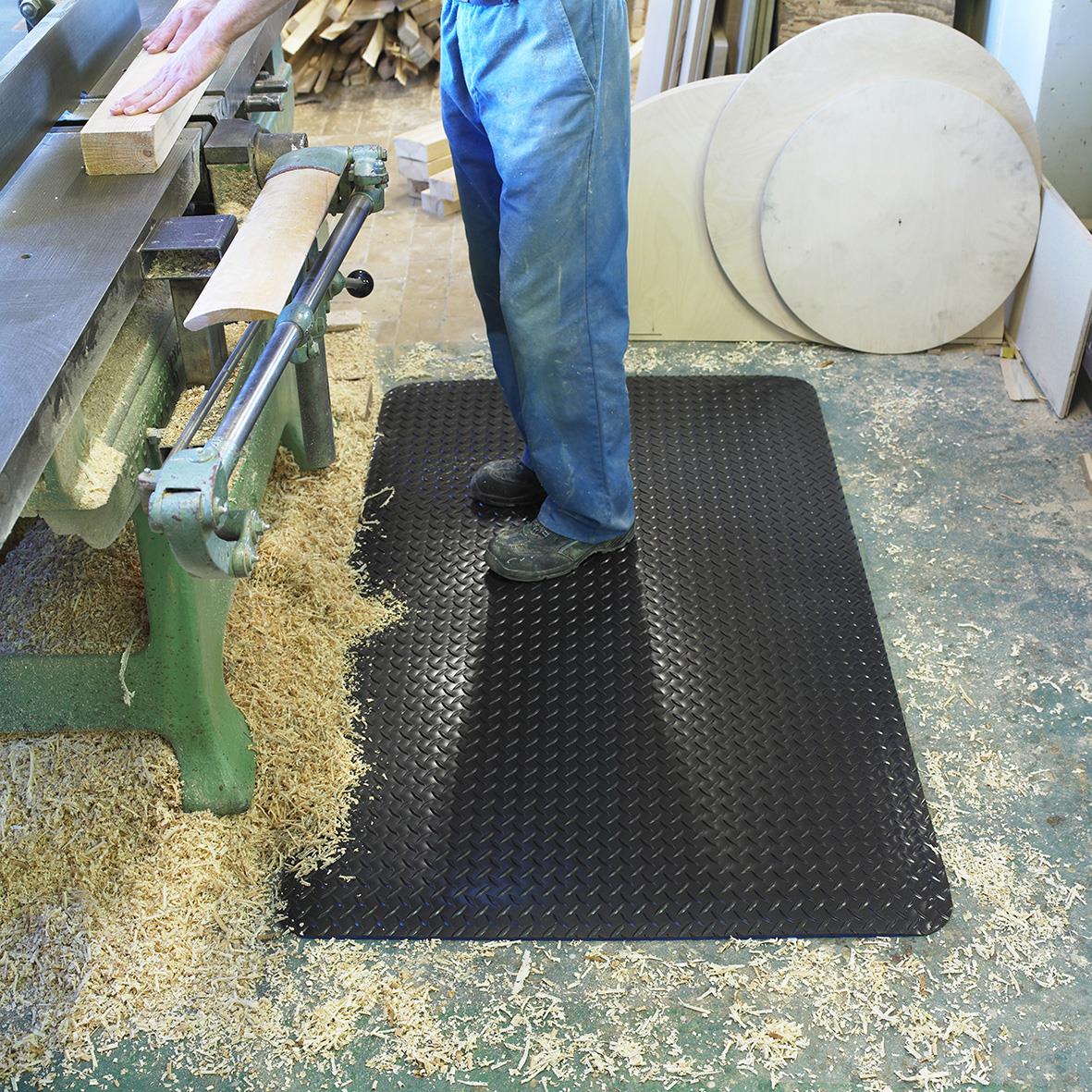 Svart arbetsplatsmatta på verkstadsgolvet med en person stående på den