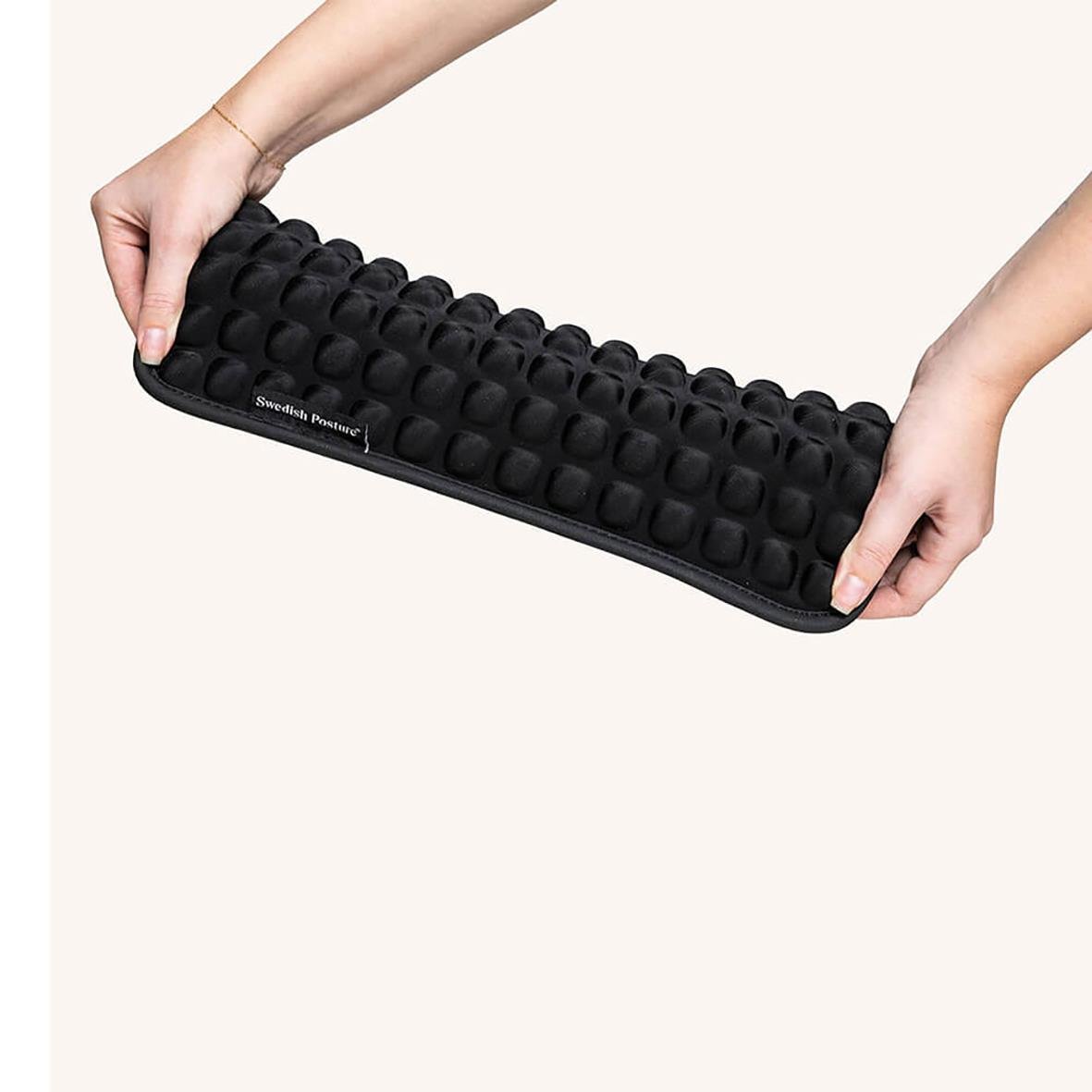 Person håller i en svart ståmatta med kuddar för att förbättra hållning och kyla