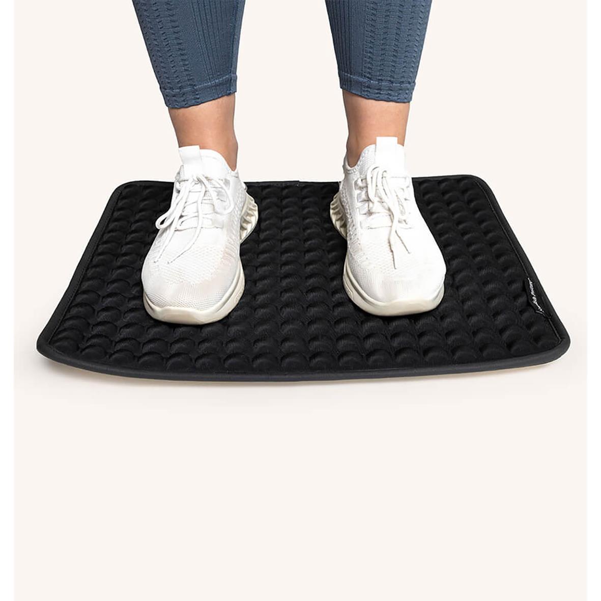 Person står på Ståmatta Swedish Posture Kylande med vita sneakers och blå jeans