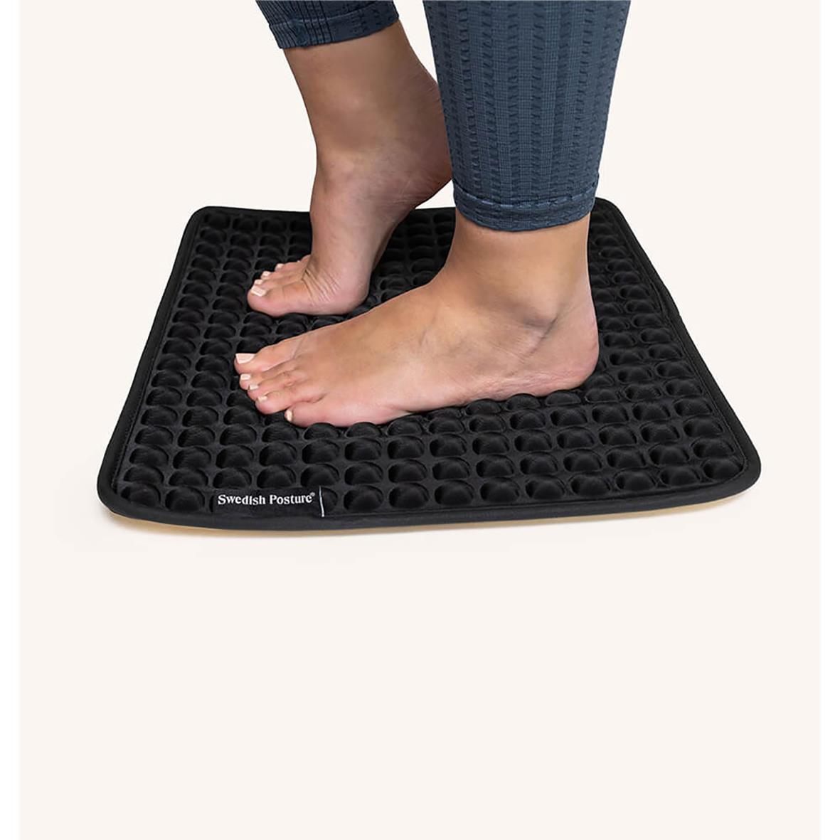 Person står på en svart ståmatta Swedish Posture Kylande med fötterna placerade på den