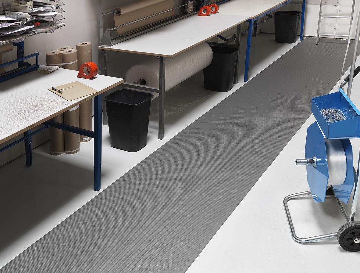 Grå arbetsplatsmatta i industriell miljö med arbetsbord och verktyg