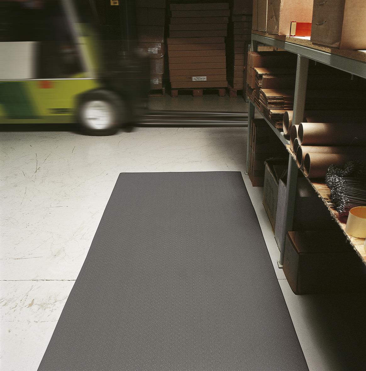 Grå arbetsplatsmatta på lager eller verkstad med hyllor och rullematerial i bakgrunden