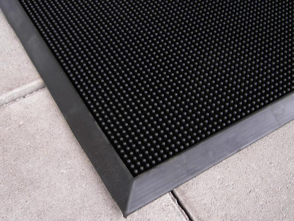 Svart gummimatta med små piggar, storlek 60x80cm, placerad vid en entrédörr på en betongyta