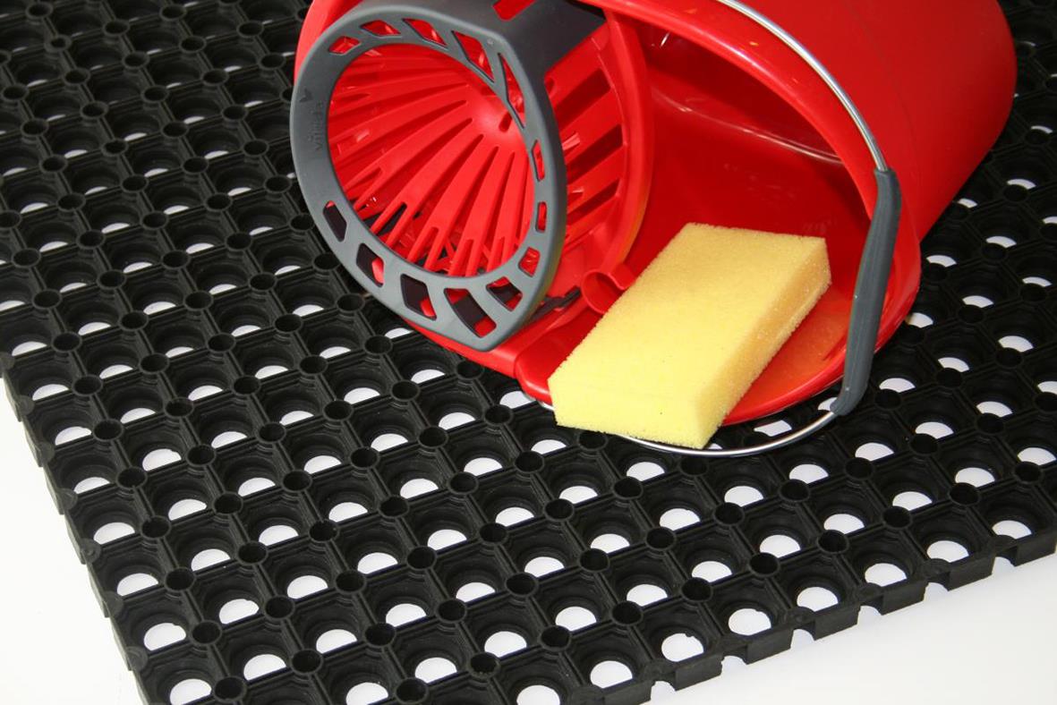 Svart gummimatta med hålmönster och en röd entrématta med rullande funktion samt en gul svamp