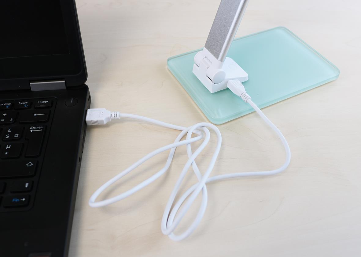 Laddare kopplad till laptop och mobil på bord med ljusgrå bordslampa Unilux Popy LED