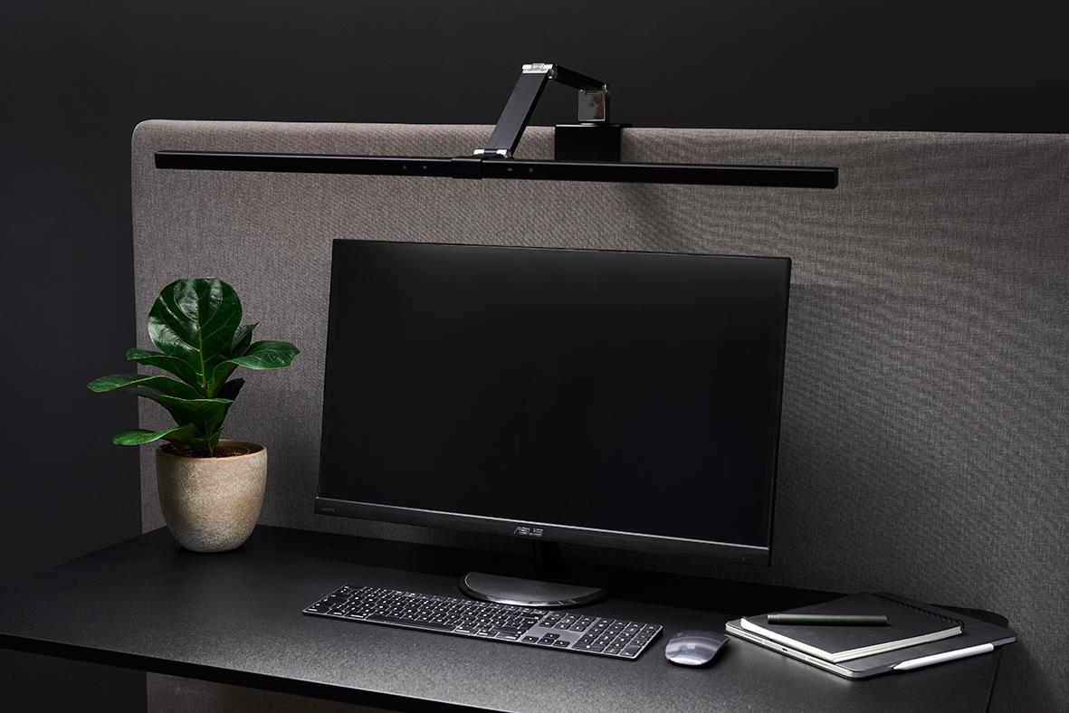 Bordslampa Sun-Flex Screenlite Panel svart bredvid datorskärm och växt på skrivbord