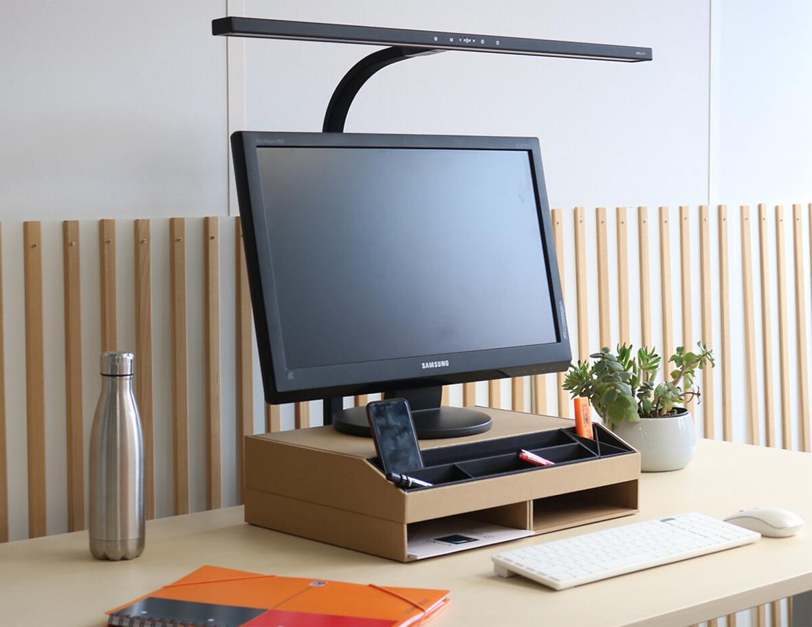 Svart skrivbordslampa Unilux Strata Lumino på ett skrivbord med dator, växt och kontorsmaterial