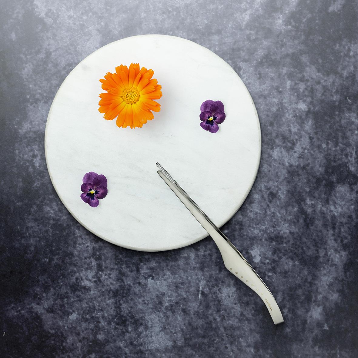 Kockpincett Global GS-107 20cm placerad på en vit marmorskiva med blommor och en tång
