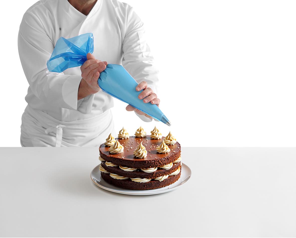 Person dekorerar en chokladtårta med grädde med en spritspåse