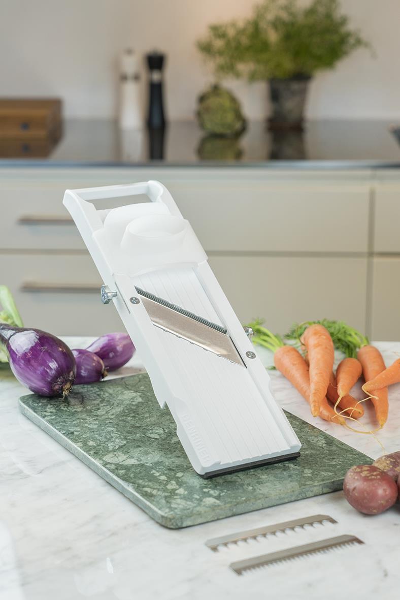Vit mandolin för grönsaksstrimling på köksbänk med morötter och lök i bakgrunden
