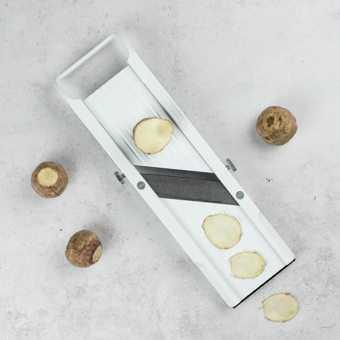 Vit mandolin Benriner med 6,4 cm blad, skivor av potatis på en yta