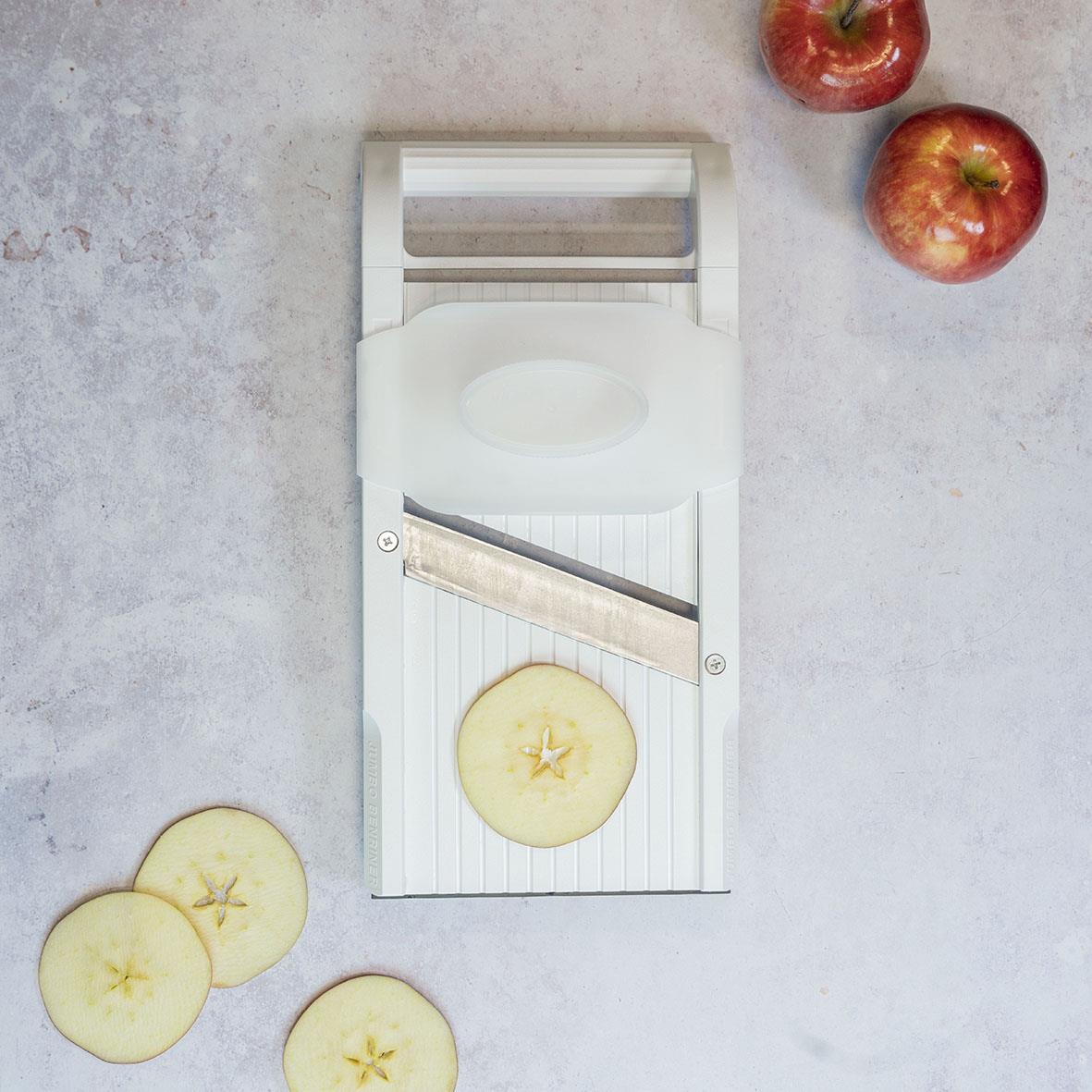 Vit mandolin för att skiva äpplen, med några skivor och hela äpplen runtom