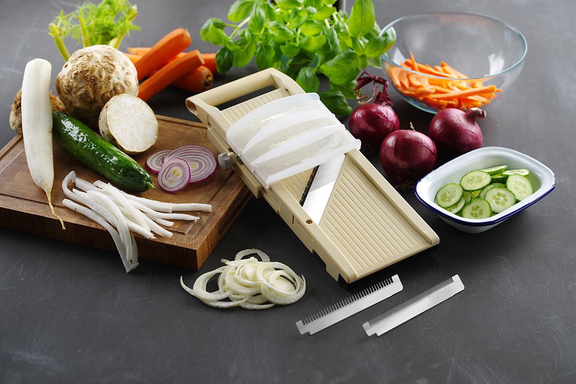 Skärbräda med grönsaker, grönsaksraffel och skivare för att göra grönsaksstrimlor