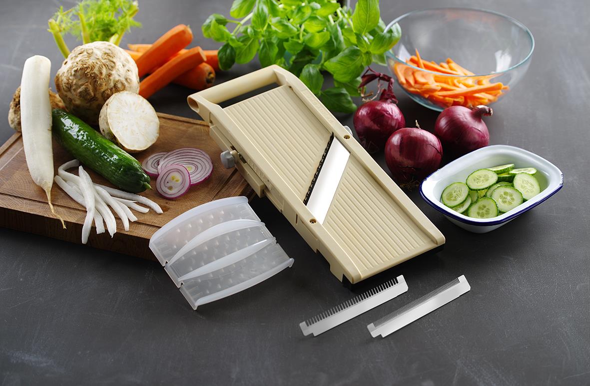 Grönsaker och en mandolin för att skära dem, inklusive morötter, lök, gurka, rödlök, och basilika