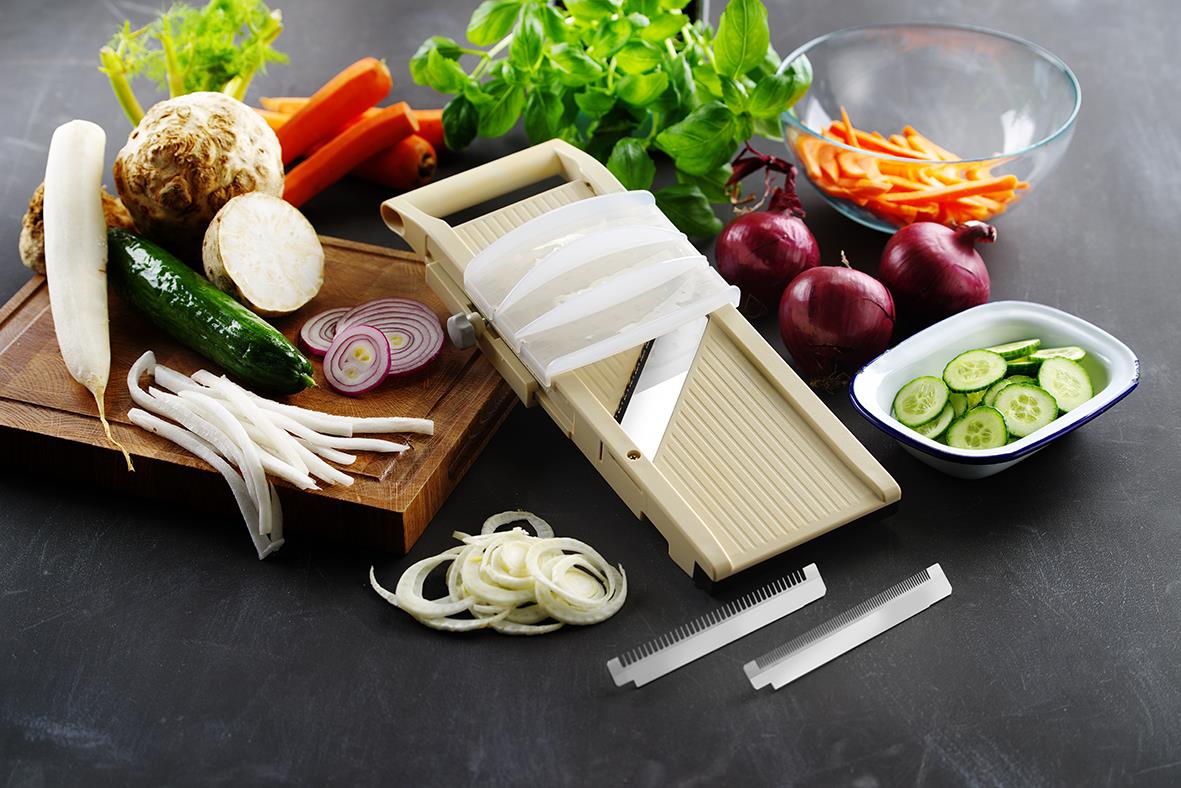 Grönsaker och en mandolin för att skära dem på ett svart bord