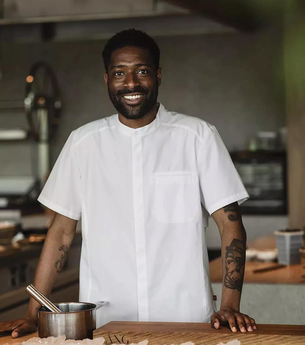 Man i vit kockskjorta med korta ärmar, står i kök och ler