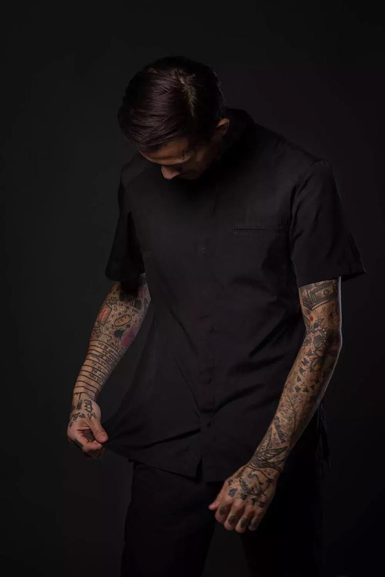 Man i mörkgrå kockskjorta med tatueringar på armarna, mörk bakgrund