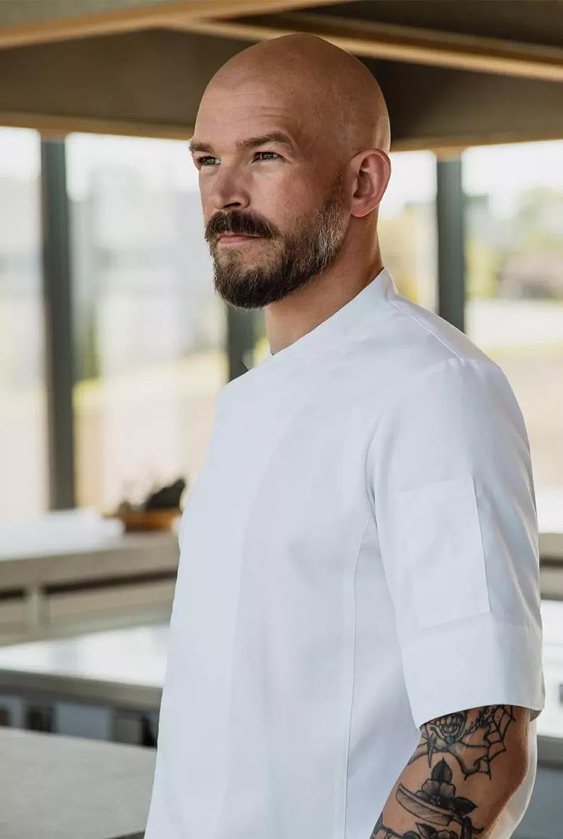 Man i vit kockrockskjorta i ett modernt kök, ser lugn och fokuserad ut