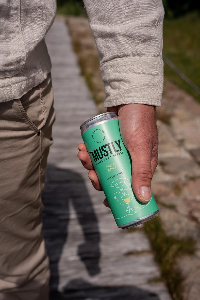 Person håller i en grön burk med Mustly äppelmust på en trästig