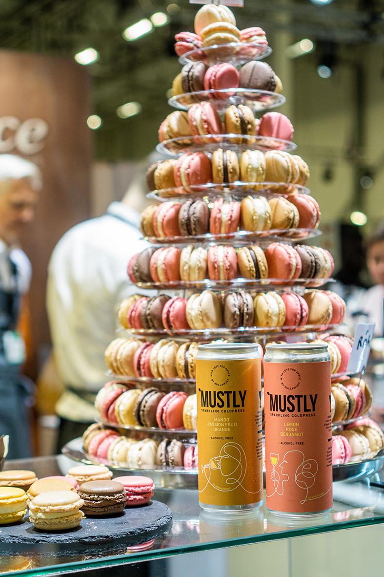 Färgglada macarons staplade i ett torn med Mustly Mango&Passion dryck i burkar framför