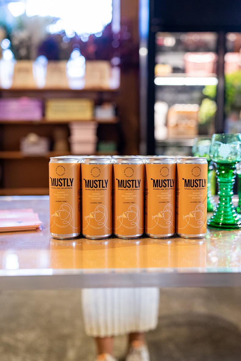 Sex burkar Mustly Mango&Passion 33cl på ett bord i butiksmiljö