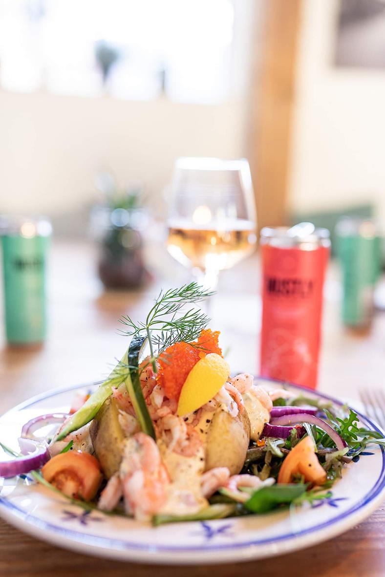 En tallrik med sallad, räkor och grönsaker, med en glas öl och en röd burk i bakgrunden, på ett träbord i ett hem eller restaurang.