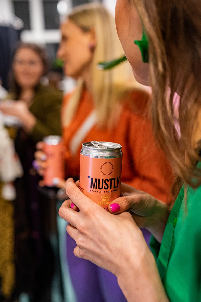 Kvinna håller i en burk med Mustly Lemon Rose dryck, omgiven av andra personer i socialt sammanhang