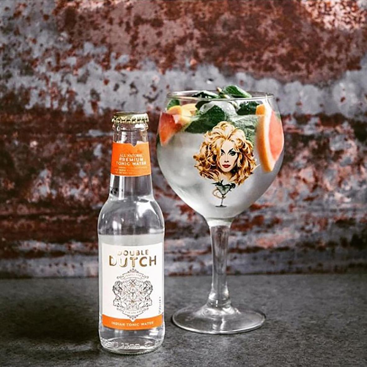 En glas med drink och en liten flaska Mixers Double Dutch Tonic Indian 20cl framför en vägg