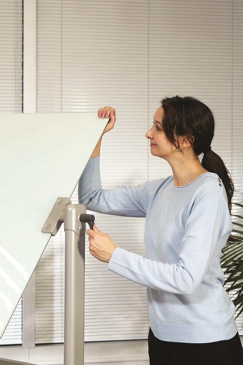 Kvinna justerar en vit magnetisk glastavla på ett stativ i ett kontorsmiljö