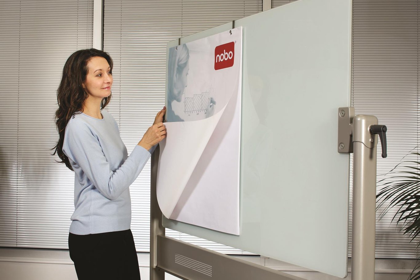 Kvinna skriver på en magnetisk vit glastavla Nobo Pivot i ett kontorsrum