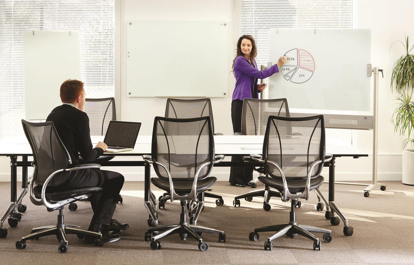 Kvinna skriver på en whiteboard i ett konferensrum med flera tomma kontorsstolar
