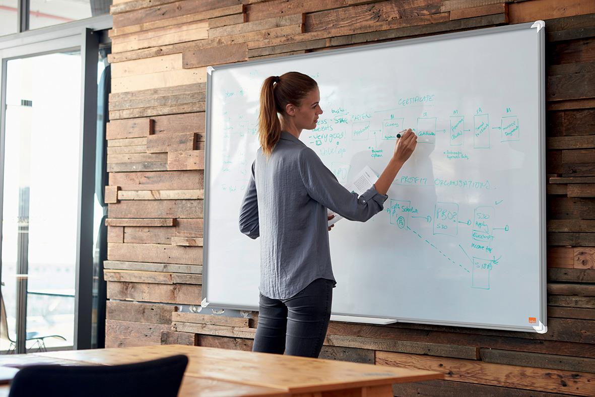 Kvinna skriver på en stor vit whiteboardtavla i ett modernt kontor med trädvägg
