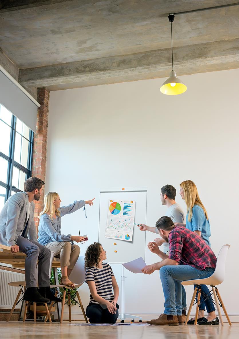 Grupp människor i ett mötesrum med en whiteboard som visar diagram och grafer, diskuterar och pekar på presentationen
