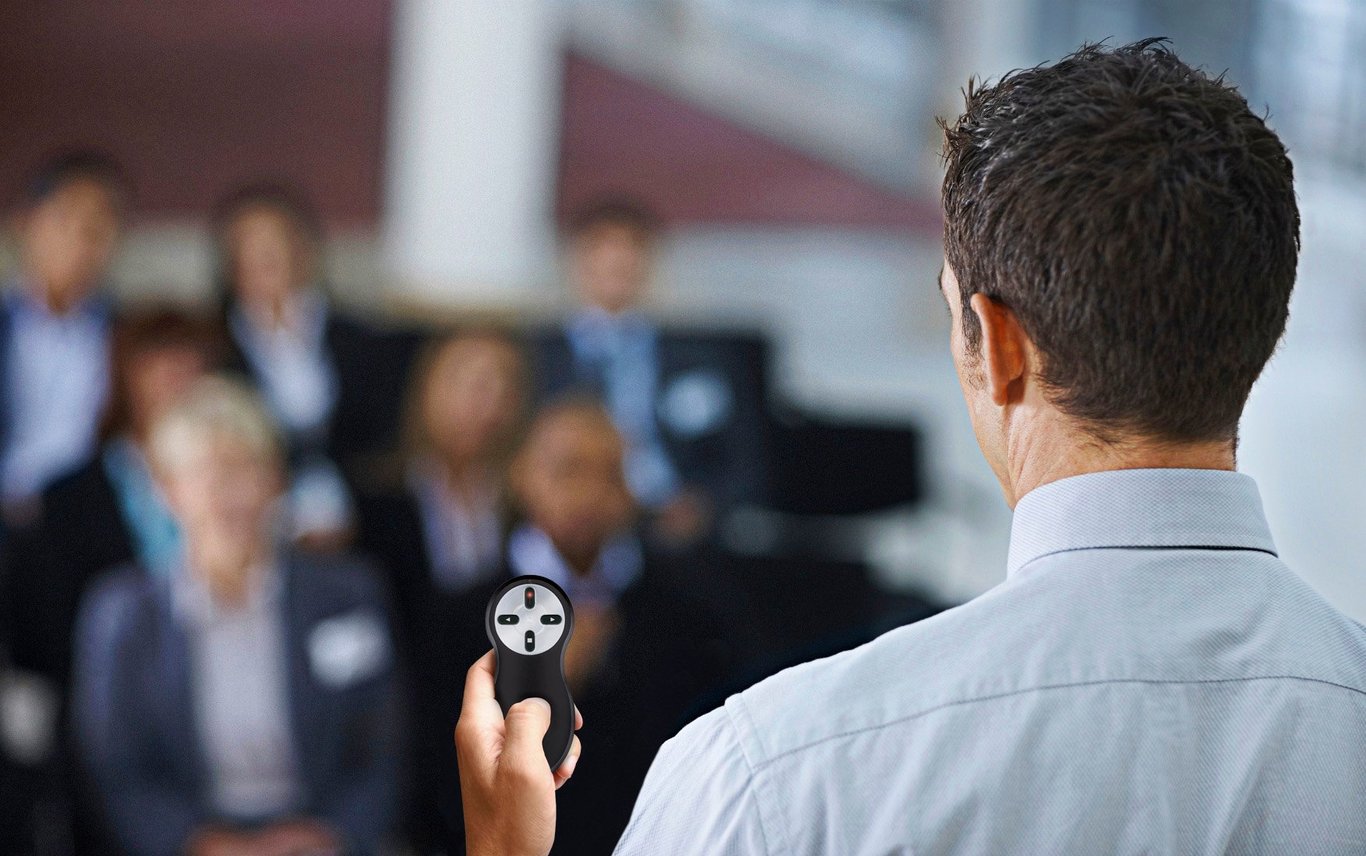 Person som håller en Kensington Röd Laser Trådlös presentationstelefon framför en publik i ett konferensrum