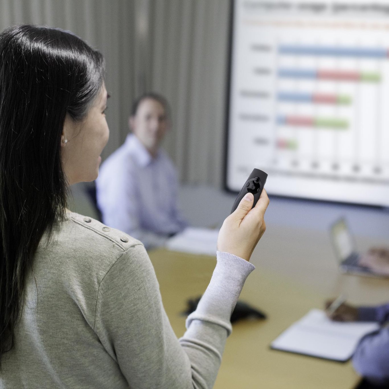 Kvinna håller en grön laserpekare framför en presentation på stor skärm i ett mötesrum