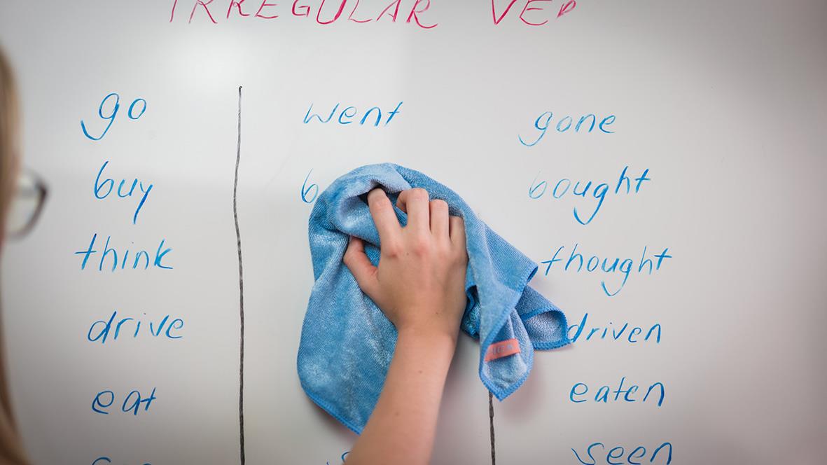 Barn torkar av en whiteboard med en blå trasa, med ord och verb på whiteboarden