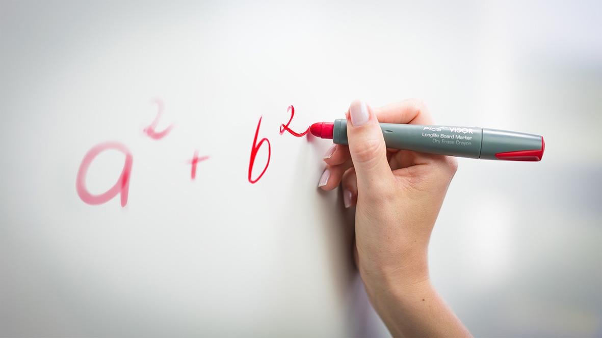 Person skriver matematiska ekvationer på en whiteboard med en röd penna