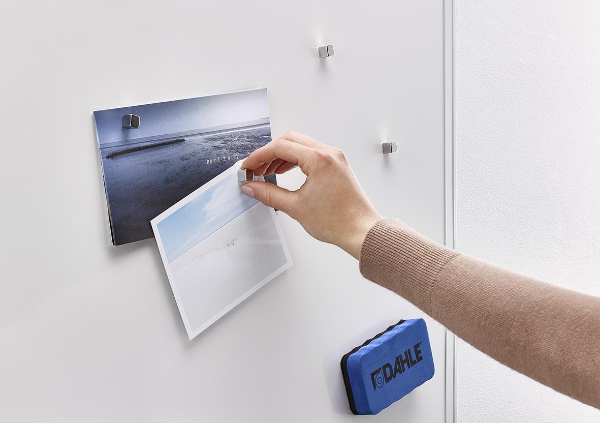 Hand som fäster ett foto på en vit kylskåpsdörr med magnet