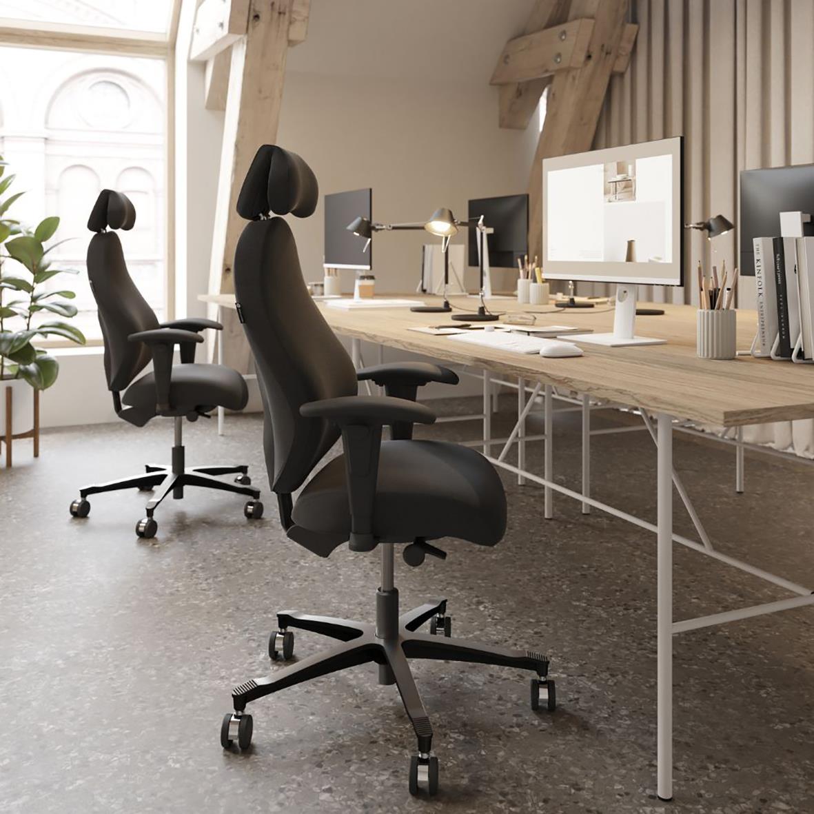 Två svarta kontorsstolar med högt nackstöd framför skrivbord med datorer i ett modernt kontorsutrymme