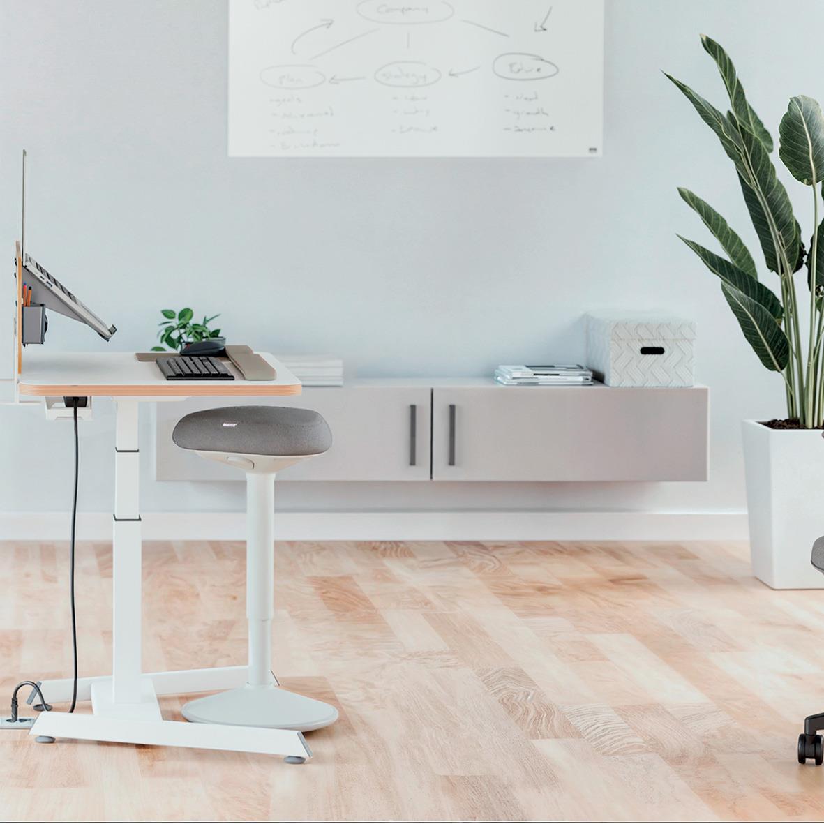 Ljusgrå stående pall Leitz Ergo Active i ett modernt kontorsutrymme med växt och skrivbord