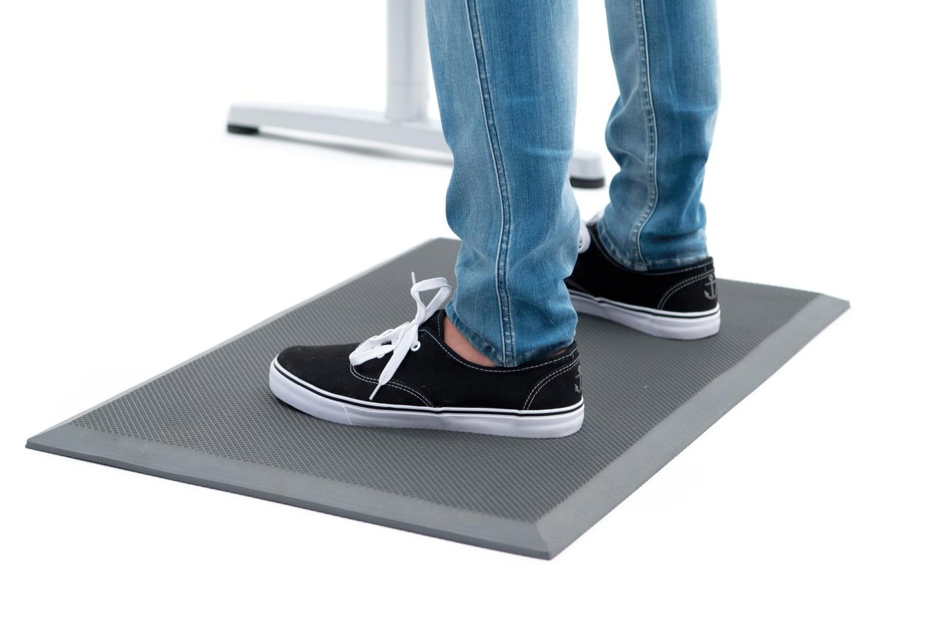 Person står på svart EVA-ståmatta med jeans och sneakers