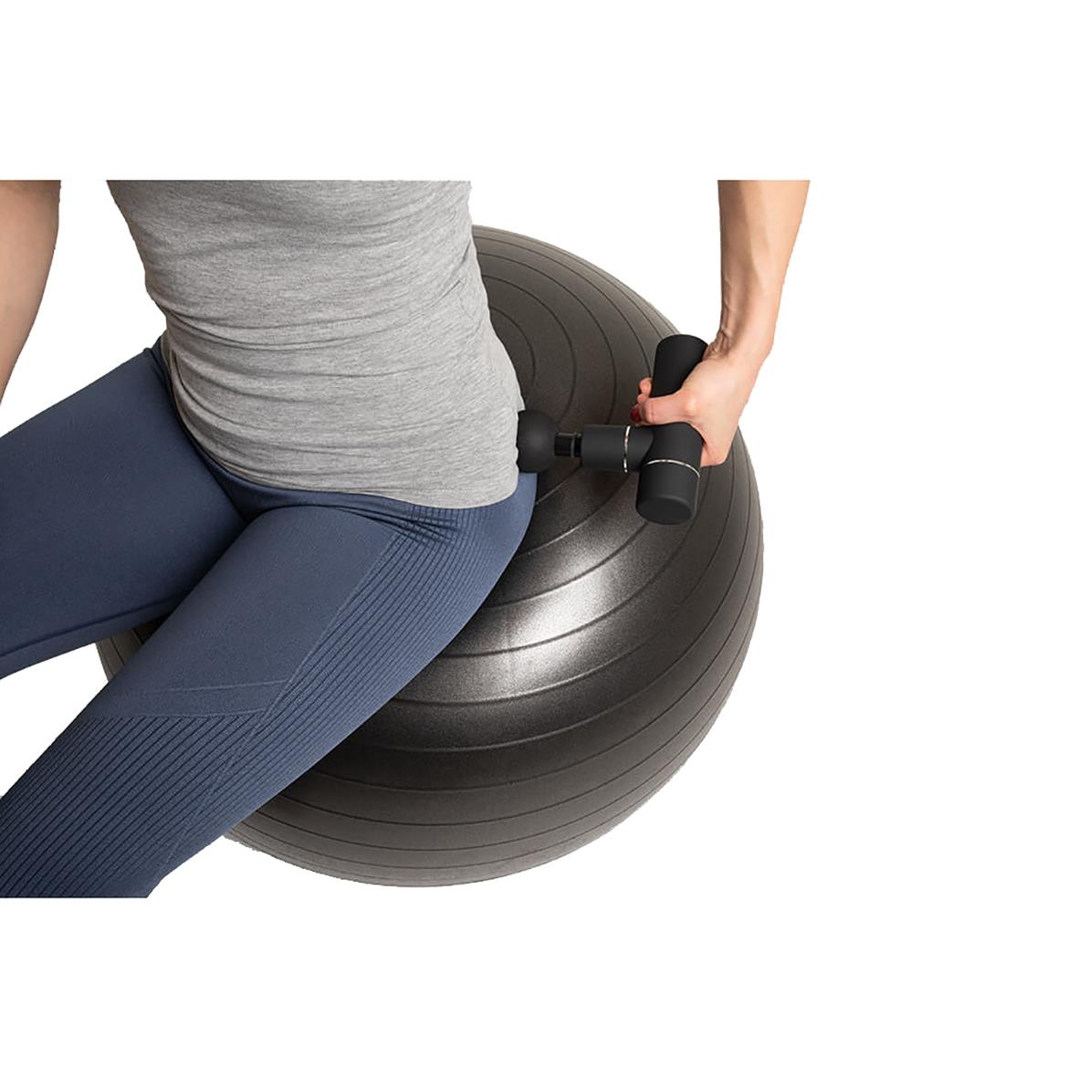 Person använder massagepistol på pilatesboll för att lindra muskelspänningar