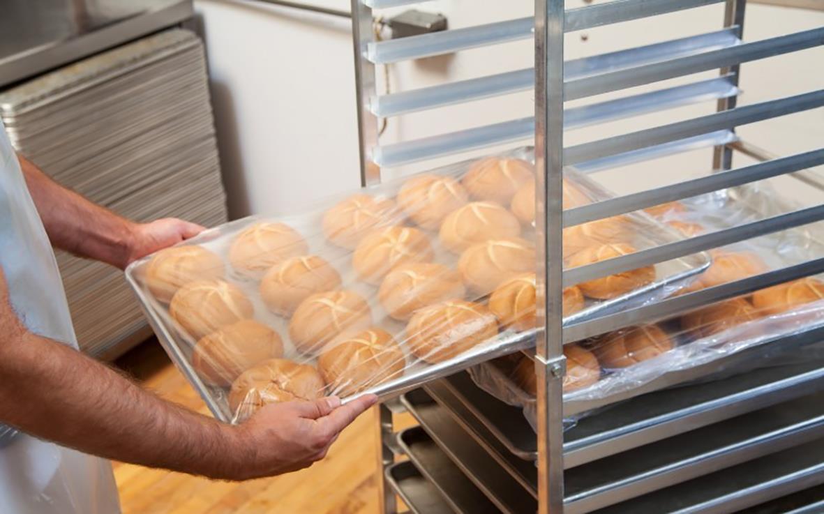Person placerar en plastpåse med bröd på ett ställ i ett bageri
