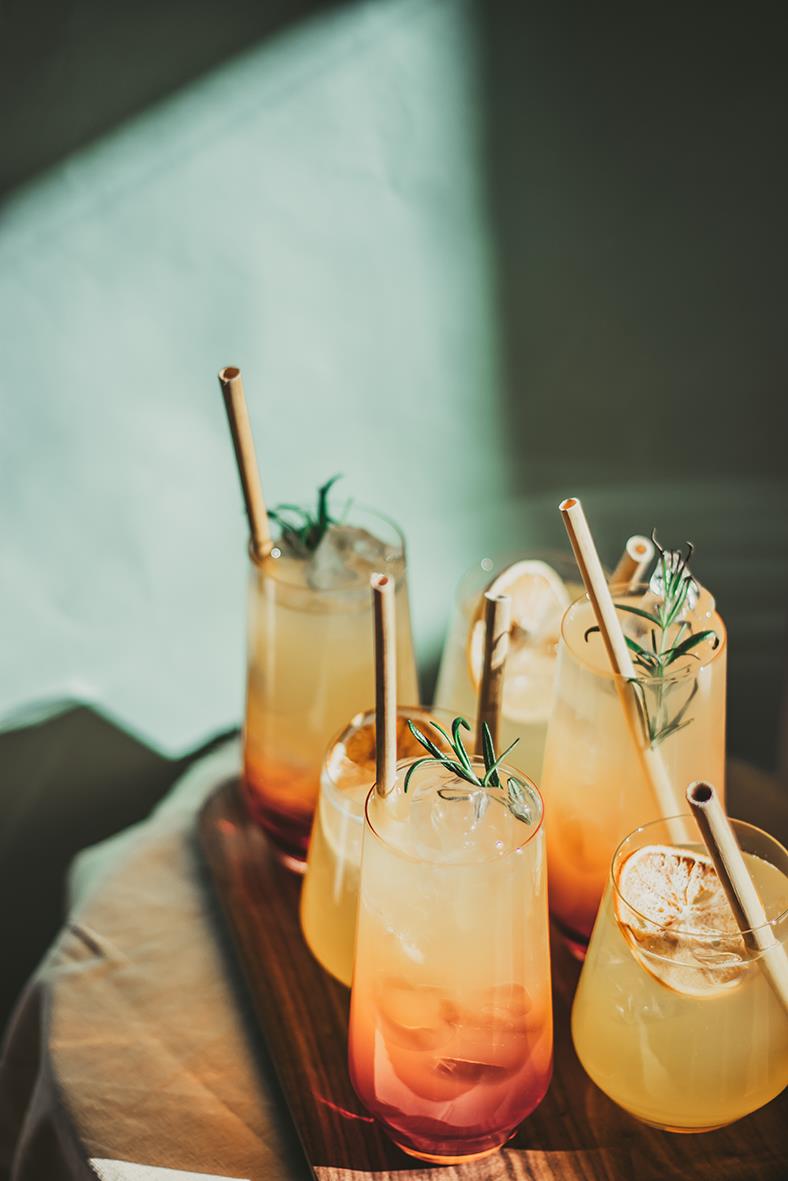 Färgglada drinkar med sugrör på ett träfat, dekorerade med örter och is